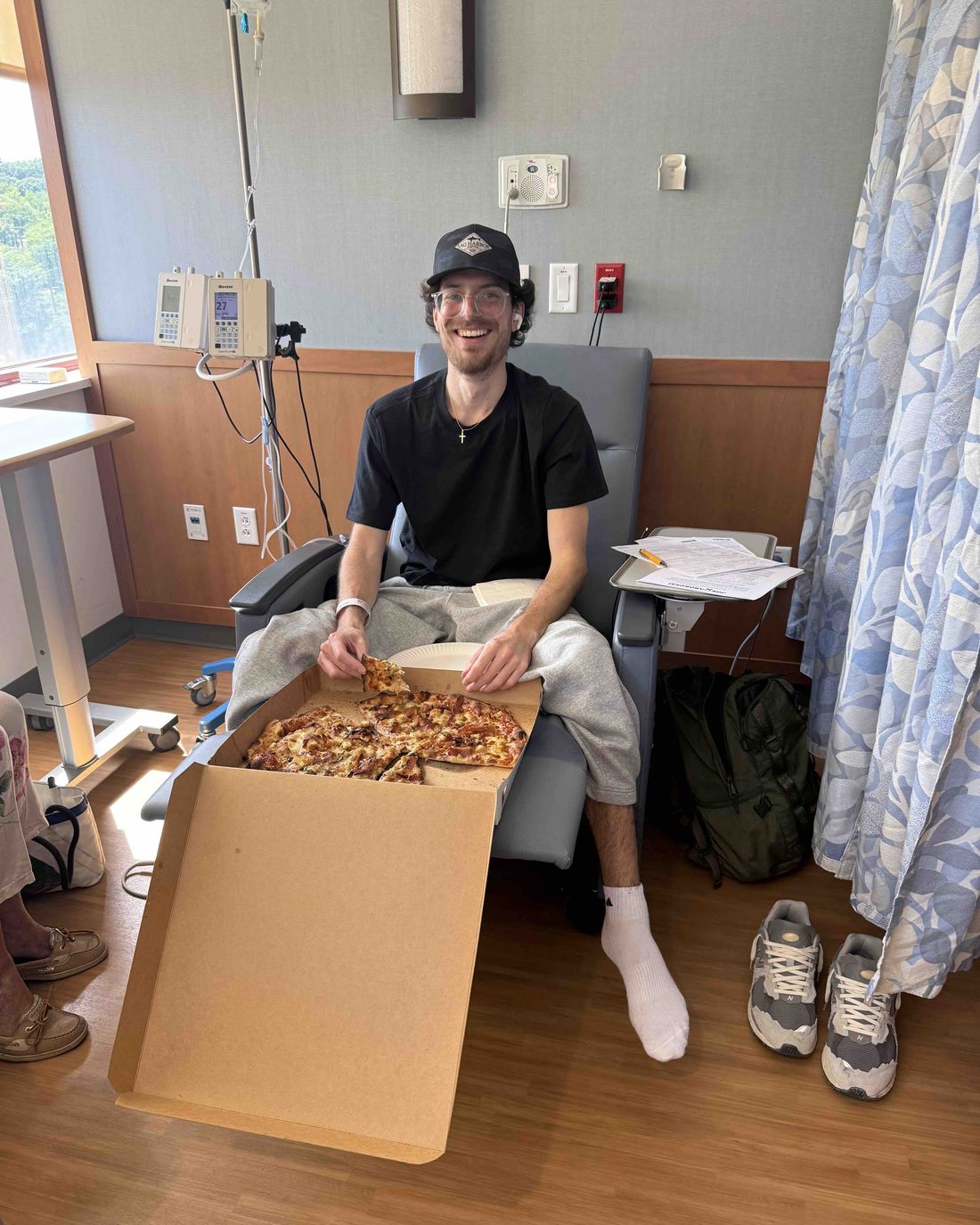 Chris smiling in an infusion chair with a pizza on his lap