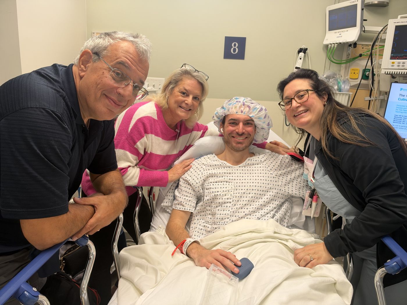 Chris smiling in his hospital bed with loved ones around him